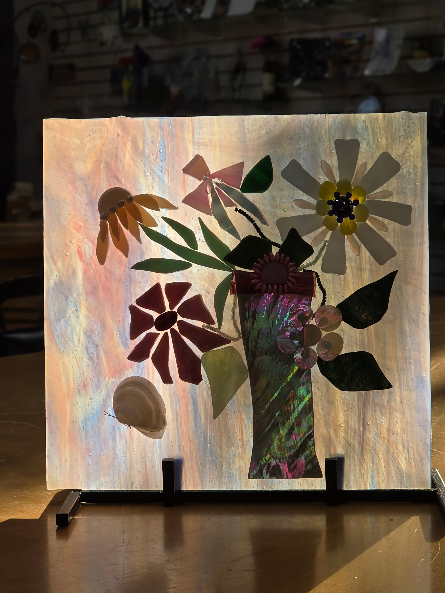 Fused glass wall panel with red, yellow, and white blossoms in a green vase on iridescent background