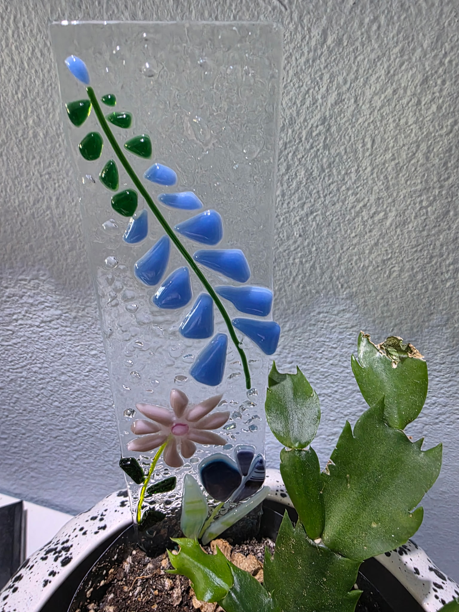 Tall clear glass vase with bell-shaped flowers transitioning from green to blue above a pink blossom