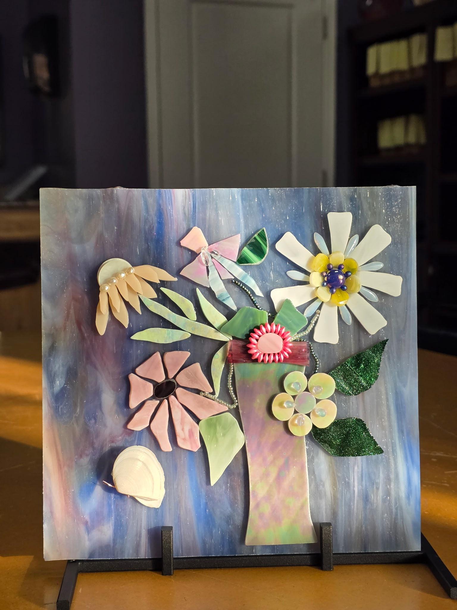 Fused glass wall panel with a stylized tree and floral elements on swirling blue iridescent background